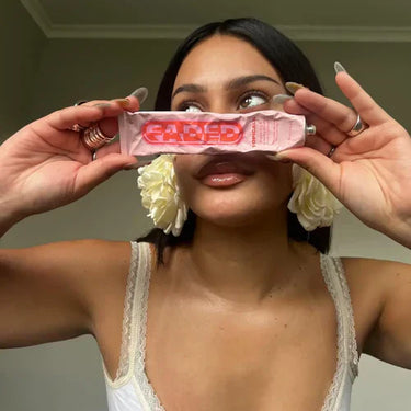 A woman holds a tube of natural scar creams, specifically Faded Topicals, in front of her face while posing stylishly